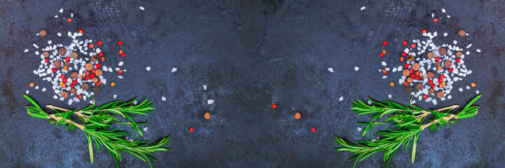 Cooking background - rosemary twig, salt, allspice, pink peppercorns on black. Top view. Wide...