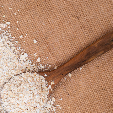 Wooden spoon with Oat flakes meal on burlap surface