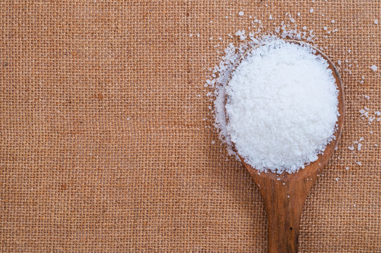 White heap of salt or sugar in wooden spoon on burlap cover surface
