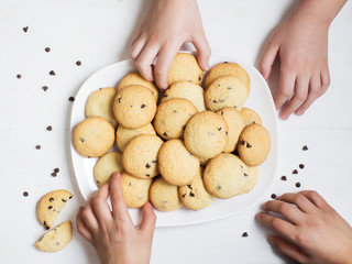 Childs hands holding American homemade cookies with chocolate drops in white plate on table