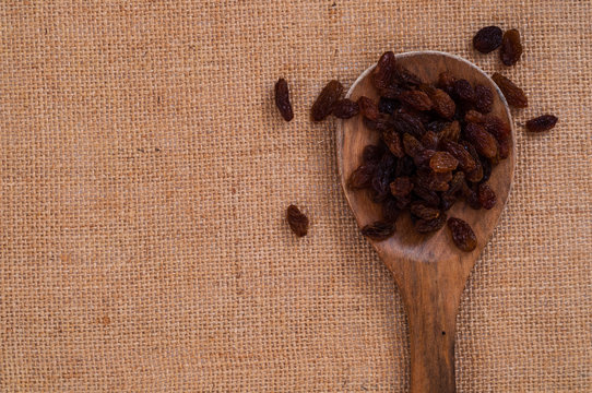 Top view into wooden spoon with heap of Raisin on burlap surface background