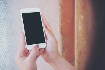 Mockup image of hand holding white mobile phone with blank black screen and vintage glass mirror background   