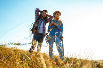 Young couple of travelers with backpacks smiling, standing in field.