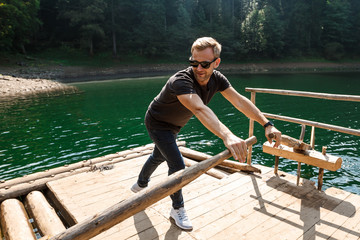 Young handsome man rowing oars in Carpathian mountains lake.