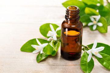 neroli essential oil in the brown glass bottle, with fresh white neroli flower and green leaves.