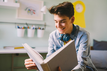 Teenage boy reading book in his room.