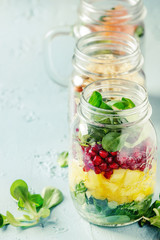 Variety of salads in mason jars. Fruit salad mango, pomegranate, greens, vegetables, wholegrain pasta, carrots and cauliflower, salmon. Standing over blue texture background. Food to go. With space