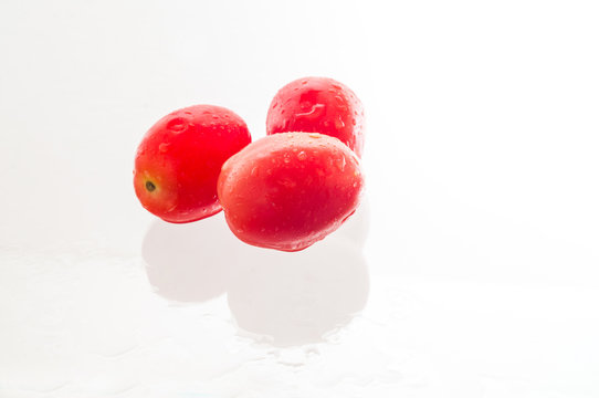 Fresh red tomatoes on wet glass table with water drops