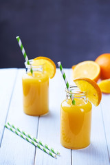 Fresh orange juice in the jar with straw on white wood table. Vertical shot