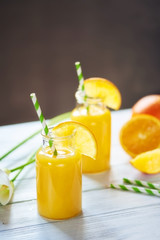 Fresh orange juice in the jar with straw and calla on white wood table. Vertical shot