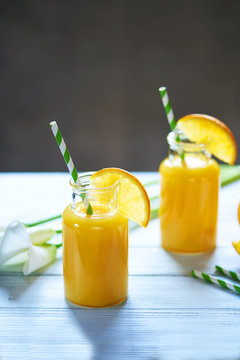 Fresh orange juice in the jar with straw and calla on white wood table. Vertical shot