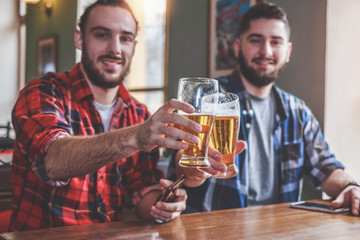 Two bearded hipsters clinking glasses of beer at bar. Cheers.