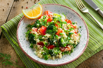 Delicious healthy meal made of couscous, broccoli and other vegetables on a rustic wooden table. Traditional eastern food. Top view.