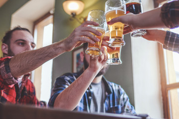 Hipster Friends cheering with beer glasses sitting around cafe bar table