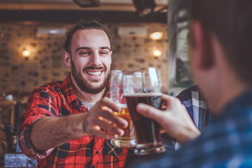 Two bearded hipsters clinking glasses of beer at bar. Cheers.
