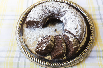 Homemade chocolate cake, with sugar glass on top, on a golden tray. Horizontal shot with natural light from a window.