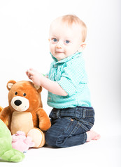 Baby Kneeling with Teddy Bear On White. a boy kneels down next to stuffed animals and looks back at camera smiling