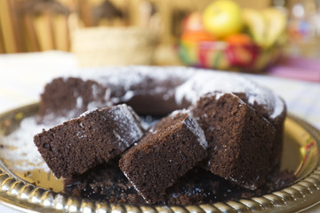 Homemade chocolate cake, with sugar glass on top, on a golden tray. Horizontal shot with natural light from a window.