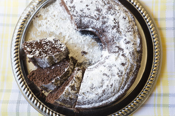 Homemade chocolate cake, with sugar glass on top, on a golden tray. Horizontal shot with natural light from a window.