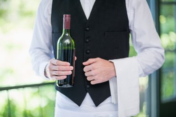 Male waiter holding bottle of wine in restaurant
