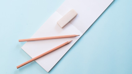 pencils, eraser and blank notebook on blue background view from above