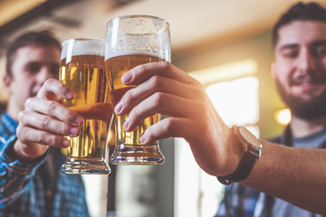 Two hipster friends clinking glasses of beer at bar