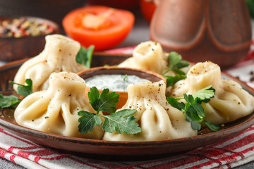 Khinkali - Georgian dumplings with meat and parsley in a ceramic dish with a sauce of sour cream and greens. Selective focus