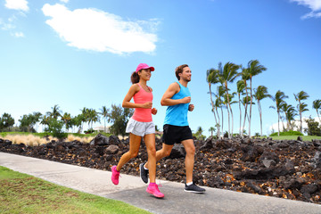Happy couple of runner friends running training for marathon race together in summer jogging on street sidewalk neighborhood park.