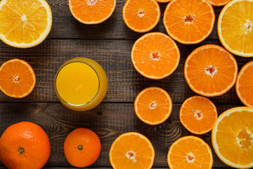 A glass of juice and cut oranges and mandarins on the wooden background