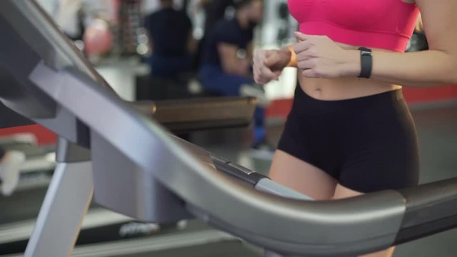 Flat tummy and slim hips of active young woman walking on treadmill in gym