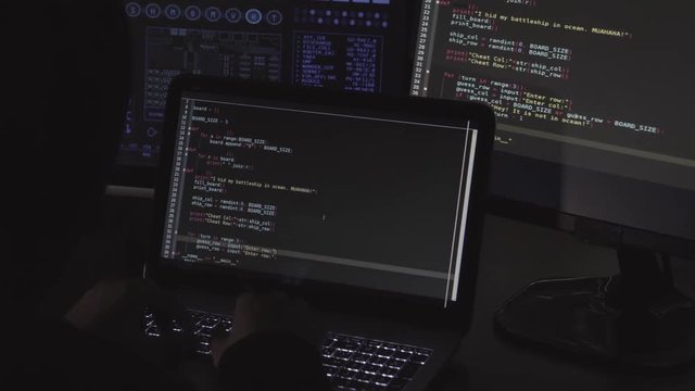 Computer hacker writing code using computers and laptop in dark room