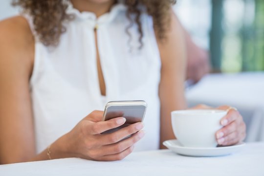 Woman holding coffee cup and using mobile phone