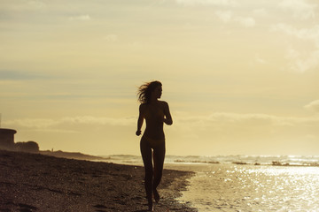 Pretty girl in yellow swimsuit running on sandy beach