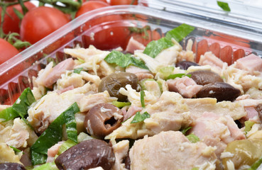 Homemade Italian chicken salad with parsley, olive oil and Cailletier or Taggiasca olives. Fresh tomatoes in the background.