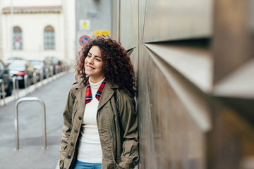 Young beautiful mixed race woman outdoor in the city leaning on a wall overlooking smiling -...