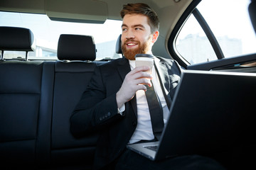 Smiling business man with laptop drinking coffee