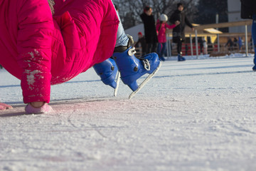 Girl in  red coat and blue figured skates fell on the ice rink