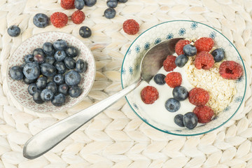 Eine Schale Müsli mit Jogurt, Hafer und Beeren, daneben ein Schälchen mit Heidelbeeren