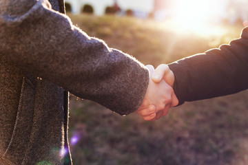 Male handshake at a business meeting outdoors. Hands close-up in backlight.