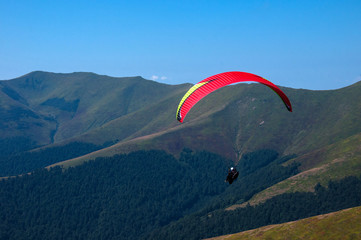 Paragliding in the sky. Paraglider fly over the tops of the mountains in summer sunny day. Carpathians, Ukraine.