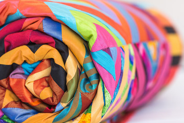 Colored patchwork quilt twisted into close up. Colorful scrappy blanket folded as background. Handmade. DOF.