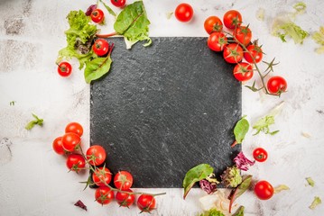 Cooking, healthy food: fresh salad leaves and tomatoes on the table, with a black cutting board, cutlery. Top view, on white concrete background