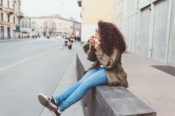 Young beautiful mixed race woman outdoor in the city eating cannolo - sweet, dessert, pastry concept