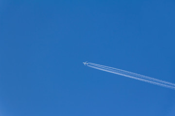 Airplane with contrails in clear blue sky