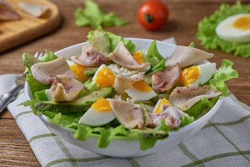 Salad of squid with egg and fresh vegetables on a wooden background
