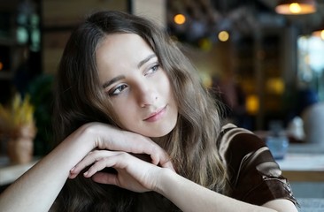 Shoulder portrait of young girl in brown blouse in cafe.