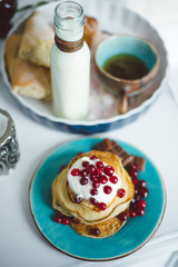 Breakfast in bed, pancakes with cream and berries, a cup of tea, a bottle of milk and a baguette on a tray