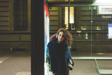 Young beautiful mixed race woman at the bus stop listening music - commuter, technology, music...