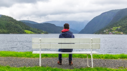 Fototapeta na wymiar Boy sitting on a bench looking at the fjord in Ulvik, Norway