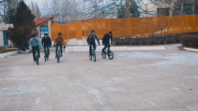 Friends of the teenagers are epically riding together on BMX and doing tricks on a winter day in the park. Slow motion. 120 fps.